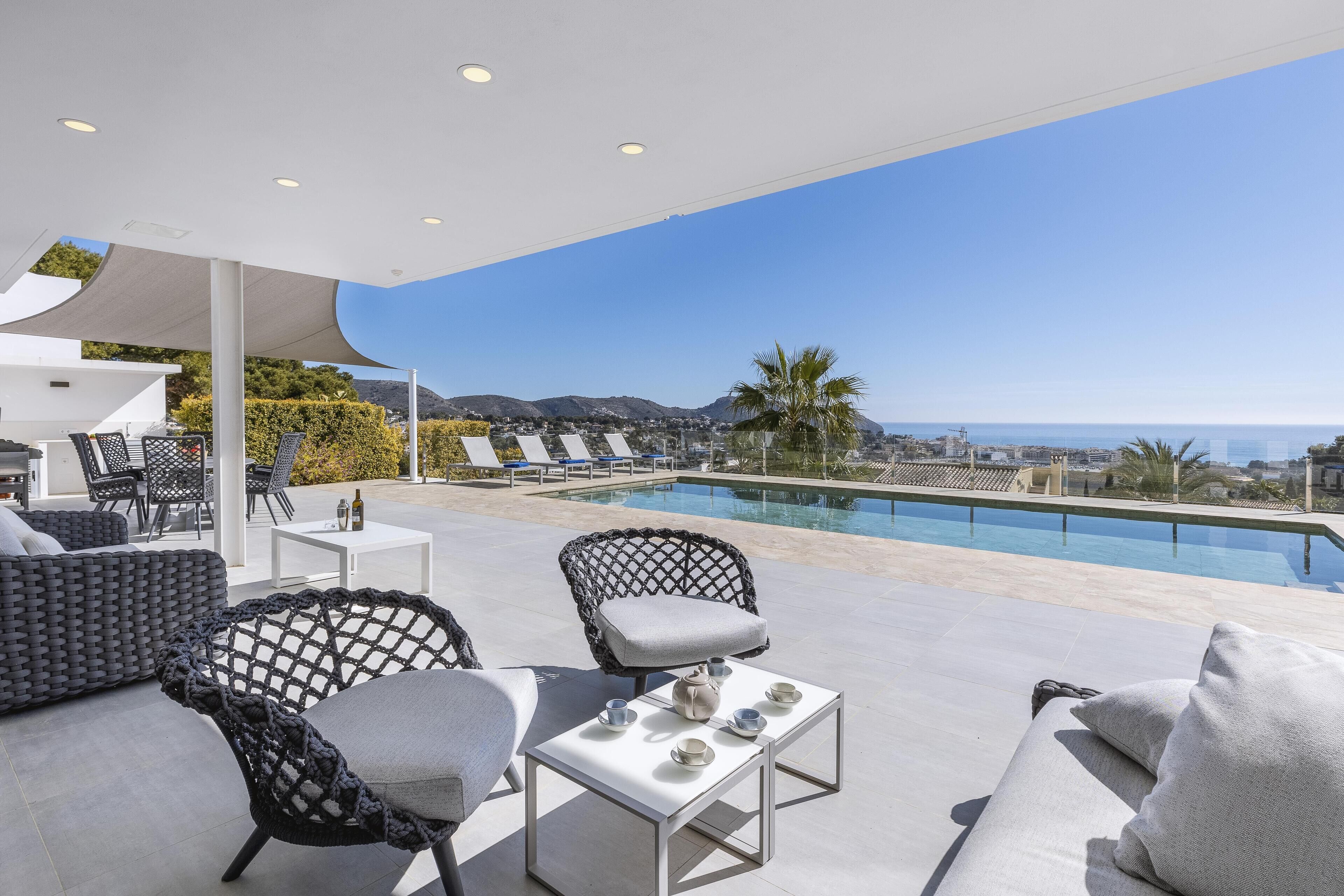 Un espace de détente extérieur moderne avec une piscine, comprenant une table blanche, deux chaises et un canapé.