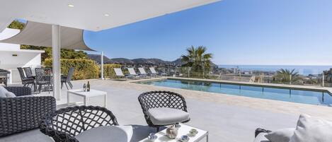 Un espace de détente extérieur moderne avec une piscine, comprenant une table blanche, deux chaises et un canapé.