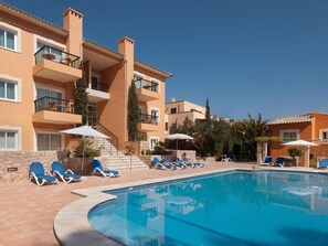 A swimming pool with lounge chairs, a staircase, and a building with balconies.
