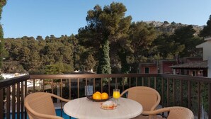 A balcony with wicker chairs, a round table, and a fruit bowl with oranges and a glass of orange juice. - Apt. Castano, community pool, close to the beach, wifi, air conditioning, (Cala Sant Vicenç)