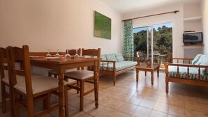 A dining area with wooden furniture, a sofa, and a television on a shelf. - Apt. Castano, community pool, close to the beach, wifi, air conditioning, (Cala Sant Vicenç)