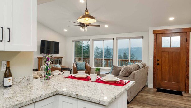 A modern kitchen with a marble countertop, a ceiling fan, and a large window overlooking a deck.