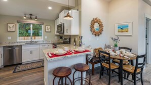 A modern kitchen with white cabinets, granite countertops, and a central island with stools. There is a dining area with a table set for four, and a large mirror on the wall.