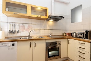 Eine moderne Küche mit Geschirrspüler, Backofen, Edelstahl-Spüle, Holzschränken und einem Fenster.