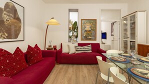 Een moderne woonkamer met een rode bank, een glazen eettafel en kunstwerken aan de muur.
