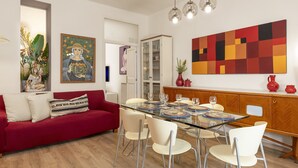 Een eethoek met een glazen tafel, witte stoelen, een rode bank en een groot abstract schilderij aan de muur.