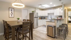 Una cocina moderna con armarios blancos, electrodomésticos de acero inoxidable y un comedor con mesa y sillas de madera.