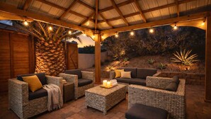 Un patio al aire libre con mobiliario de mimbre, una palmera y luces colgantes.