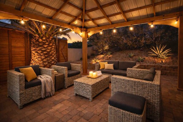 Eine Terrassengruppe mit Korbmöbeln, einer Steinwand und Lichterketten.