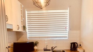Cocina pequeña con armarios blancos, encimera de madera, horno empotrado, fregadero y lámpara colgante.