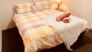 Una cama bien hecha con un edredón a cuadros, una toalla enrollada y una almohada decorativa.