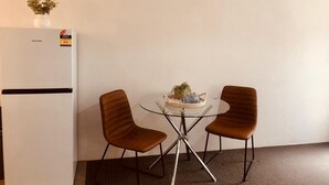 Una habitación compacta con un refrigerador blanco, dos sillas marrones, una mesita con una planta y una alfombra.