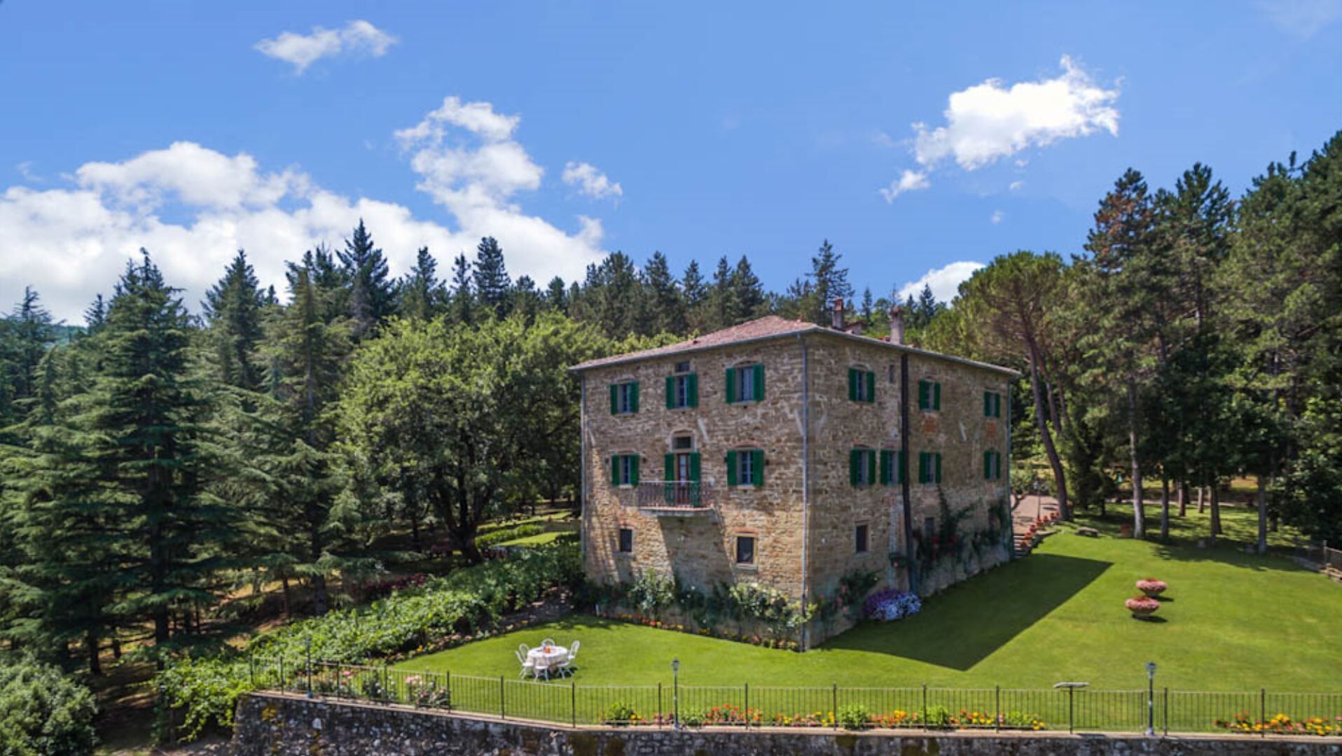 A stone building with green shutters, surrounded by a well-maintained lawn and trees.