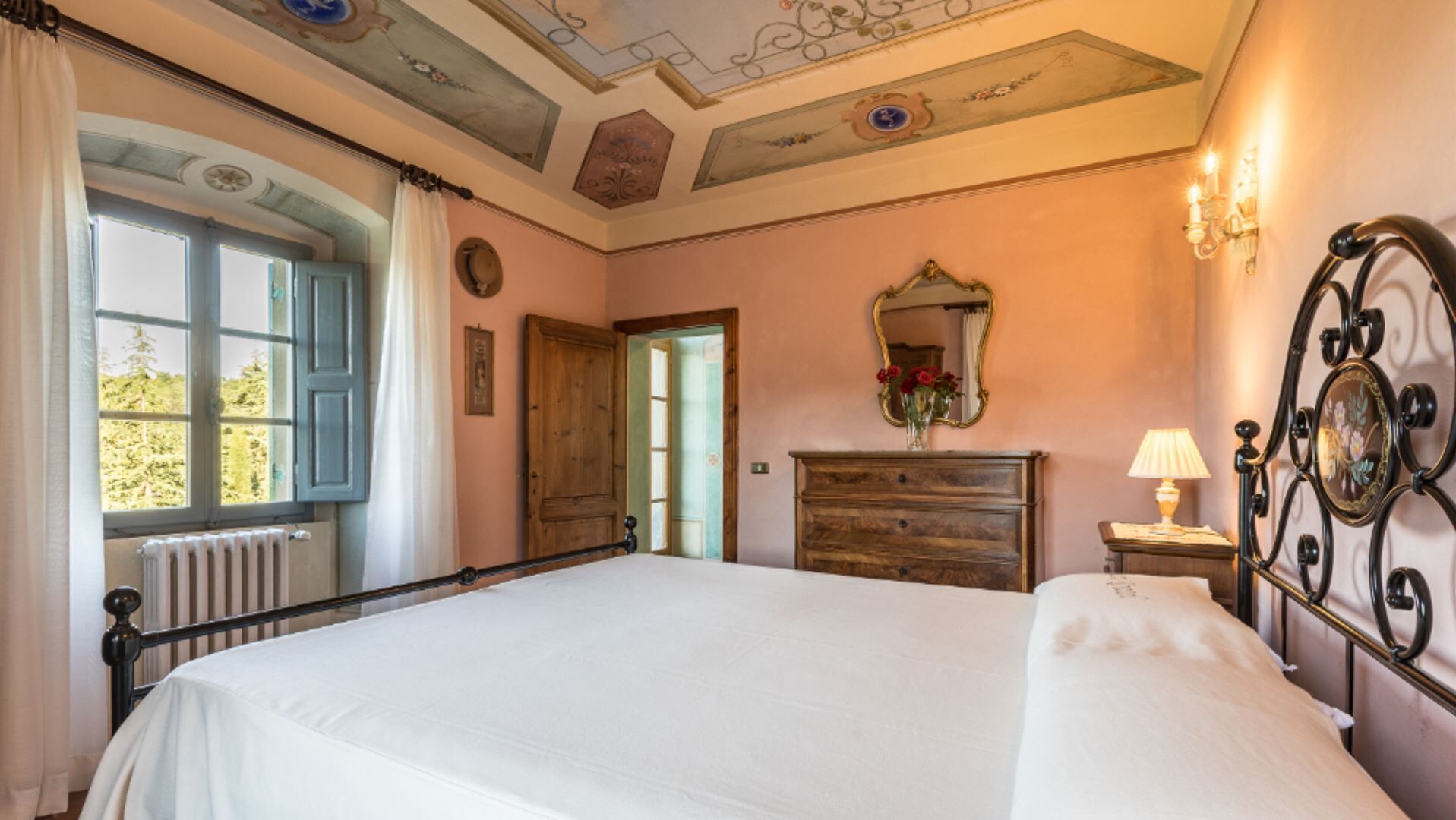 A bedroom with a large bed, a wooden dresser, a mirror, and a window with curtains.