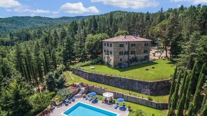 Edificio de piedra con piscina y zona de estar exterior, rodeado de un paisaje boscoso.