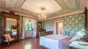 Un dormitorio con una cama grande, una silla de madera, un aparador y un espejo.