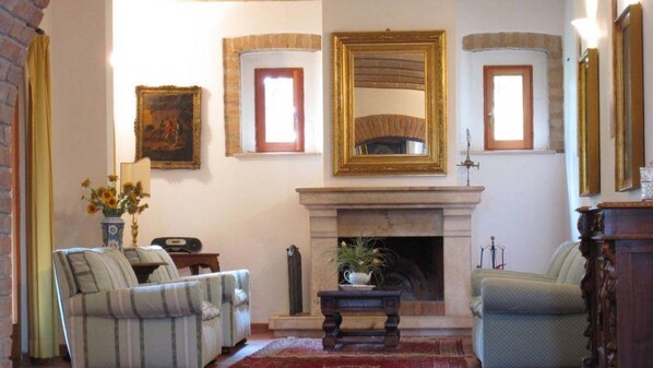 A traditional living room with a fireplace, two armchairs, a coffee table, and a painting on the wall.