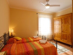 A room with two beds, a wooden wardrobe, a ceiling fan, and a window with curtains.