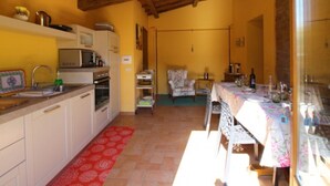 A compact kitchen with white cabinets, a microwave, and a sink. There is a dining area with a table set for two and a chair. - MULINO DELLA RASSINA - MULINO DELLA RASSINA (Arezzo)