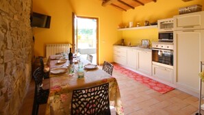 A dining area with a table set for four, a stone wall, and a kitchen with white cabinets and appliances. - MULINO DELLA RASSINA - MULINO DELLA RASSINA (Arezzo)