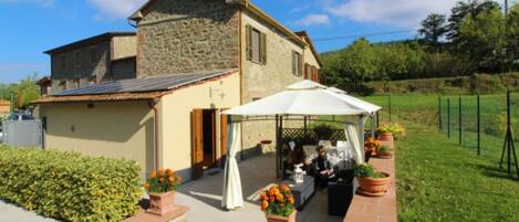 A stone house with a patio area, a white umbrella, and potted plants.