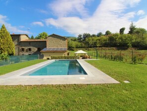 A rectangular swimming pool with a paved deck, surrounded by a grassy lawn.