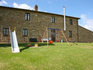 A stone building with a grassy yard, a swing set, and a slide.