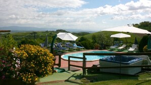 Zona de piscina con sillones reclinables y sombrillas, rodeada de vegetación y colinas.
