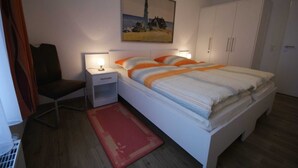 A bedroom with a bed, nightstands, a chair, a painting, and a wardrobe. - HLI 3.13 4 persons 77sqm - Residence Hohe Lith Cuxhaven (3.1.1) (Cuxhaven)