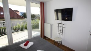 Quarto de hotel com cama, televisão presa na parede, radiador e varanda com grade.