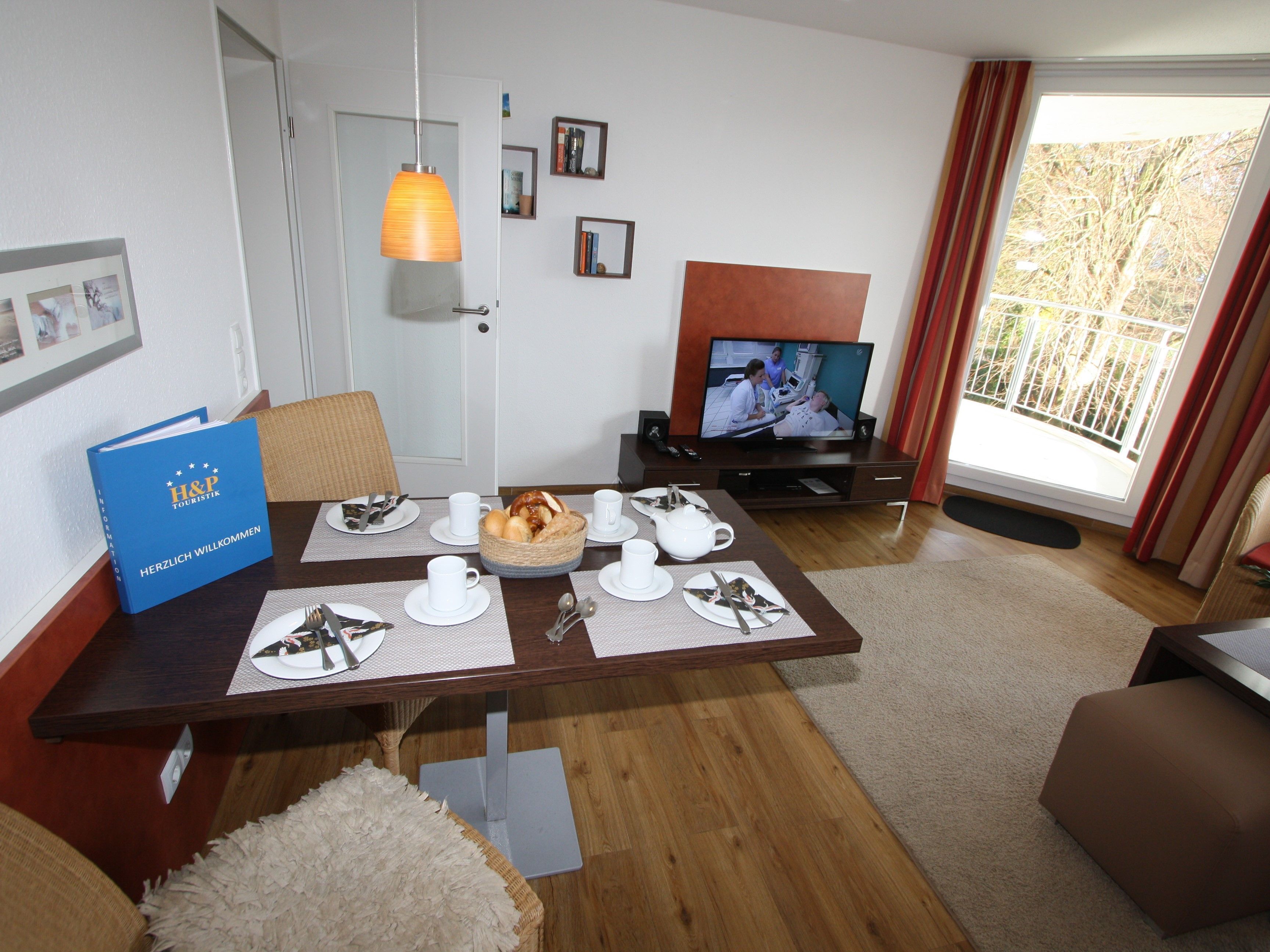 A hotel room with a dining table set for breakfast, a television, and a large window with curtains.
