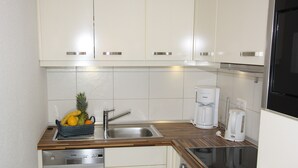 Cozinha compacta com pia, cafeteira, forno embutido e uma cesta de frutas.