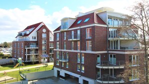 Un immeuble résidentiel à plusieurs étages, doté de balcons, d’une aire de jeux et d’un espace de stationnement.