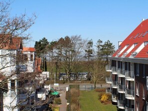 Un edificio residenziale con diversi balconi, un tetto rosso e vista su un parco con alberi e un sentiero.