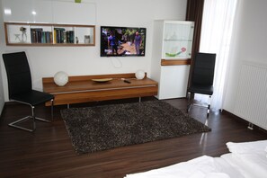 Una camera d'albergo moderna con una panca in legno, due sedie nere, un televisore e una libreria.