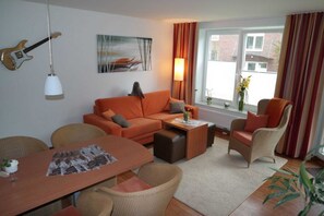 Ein Wohnzimmer mit einer Couch, Sesseln, einem Couchtisch und einem Esstisch.