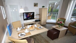Ein modernes, helles Zimmer mit Essbereich, Fernseher und Blick ins Freie.