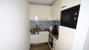 Una cocina compacta con armarios blancos, encimera de madera, horno integrado y microondas.