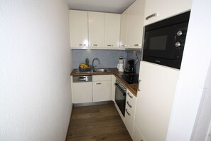 A compact kitchen with white cabinets, a wooden countertop, a built-in oven, and a microwave.