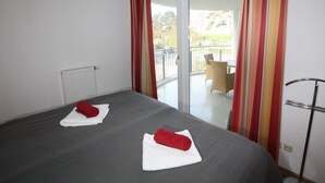 Ein Hotelzimmer mit Bett, zwei Handtüchern, einem Heizkörper und Blick auf einen Balkon mit Stuhl und Tisch.