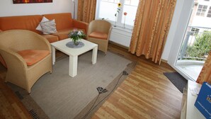Un soggiorno con divano, poltrone, tavolino da caffè e vista all'esterno attraverso una finestra.