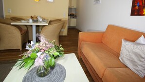 Un soggiorno con un divano arancione, una zona pranzo con sedie in vimini e una cucina sullo sfondo.
