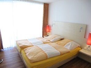 Un lit double avec une couvre-lit jaune et deux oreillers, une table de chevet avec une lampe et une fenêtre avec des rideaux.