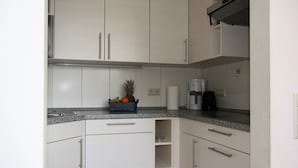 Een moderne keuken met witte kasten, een granieten aanrecht, een koffiezetapparaat en een fruitmand.