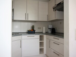 A modern kitchen with white cabinets, a granite countertop, a coffee maker, and a fruit basket.