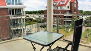 Een balkon met een glazen tafel en stoel, met uitzicht op een parkeerplaats en gebouwen met rode daken.