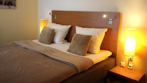 A neatly made bed with a wooden headboard, two bedside lamps, and a painting on the wall. - HLI 1.11 up to 6 people 69sqm - Residenz Hohe Lith Cuxhaven (1.1) (Cuxhaven)