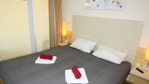 A hotel room with a large bed, two white pillows, and two red towels. There is a nightstand with a lamp and a remote control. - HLI 1.22 4 persons 48sqm - Residence Hohe Lith Cuxhaven (1.2) (Cuxhaven)