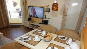 A dining area with a TV, wicker chairs, a buffet table, and a door. - HLI 1.22 4 persons 48sqm - Residence Hohe Lith Cuxhaven (1.2) (Cuxhaven)