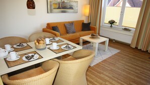 A furnished living room with a sofa, dining table, and wicker chairs. - HLI 1.22 4 persons 48sqm - Residence Hohe Lith Cuxhaven (1.2) (Cuxhaven)